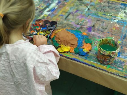 Kind in Malkittel mit bunten Farben