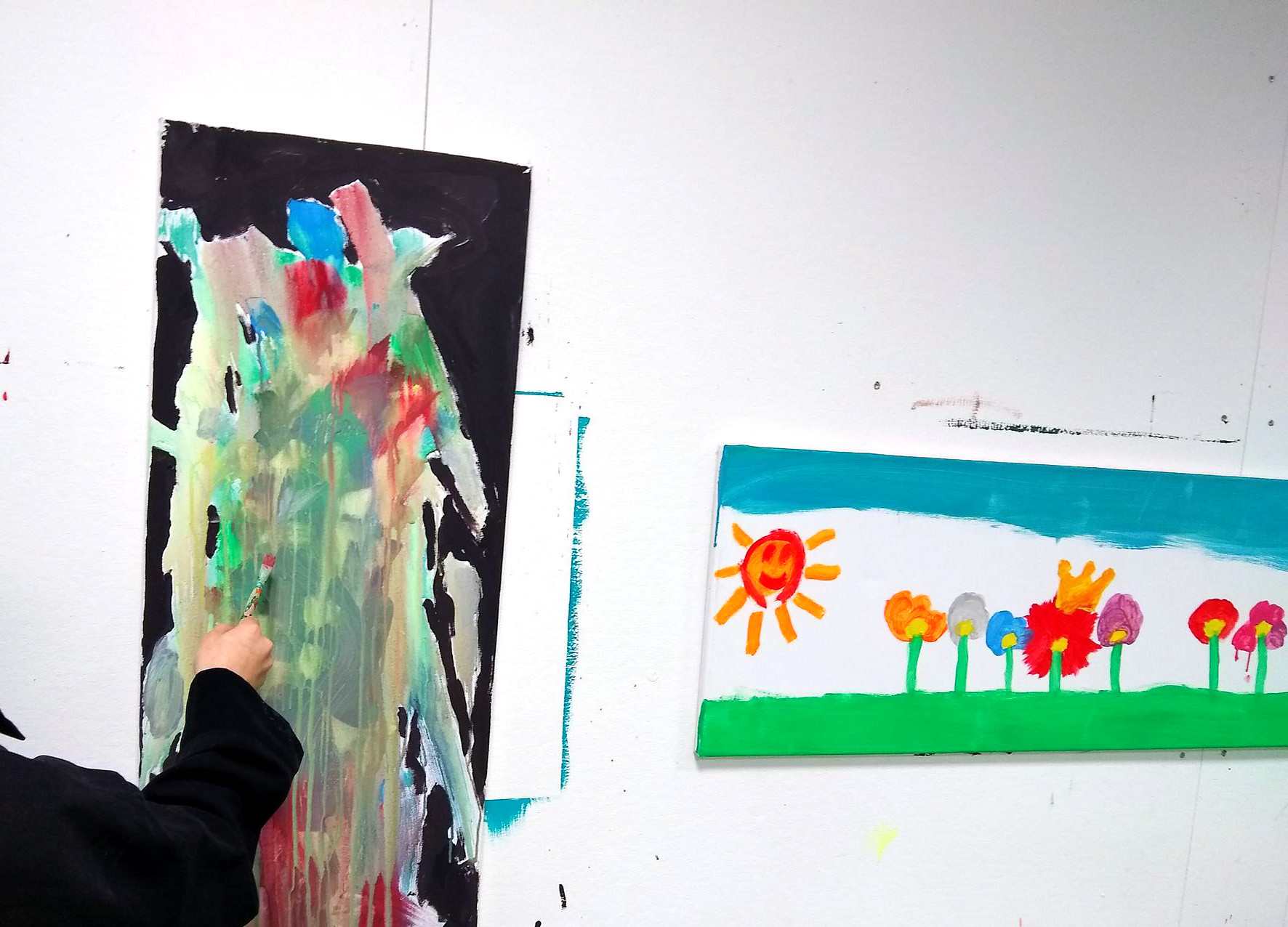 Kind malt im Stehen an der Wand ein abstraktes Bild mit leuchtenden Farben
