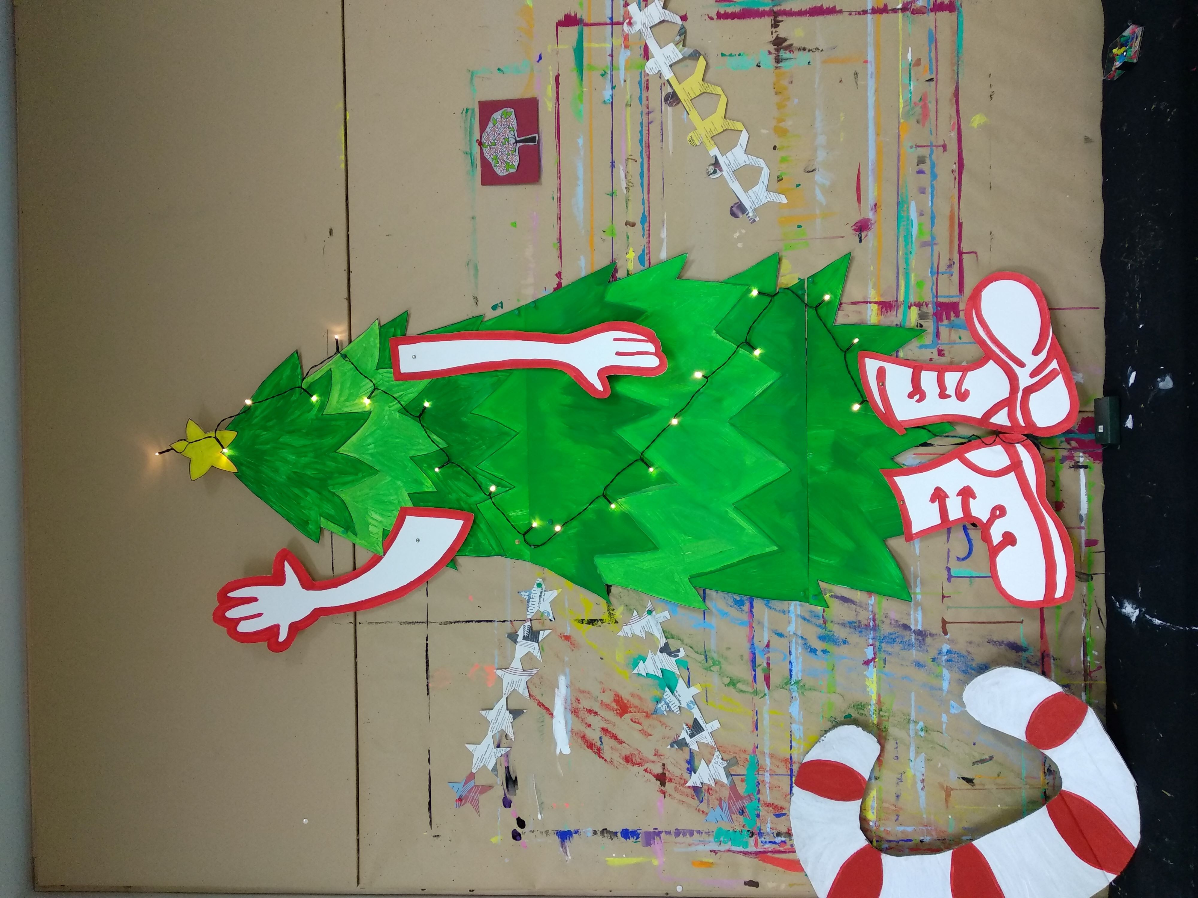 großer Weihnachtsbaum aus Papier, mit Armen und Stiefeln, winkend.