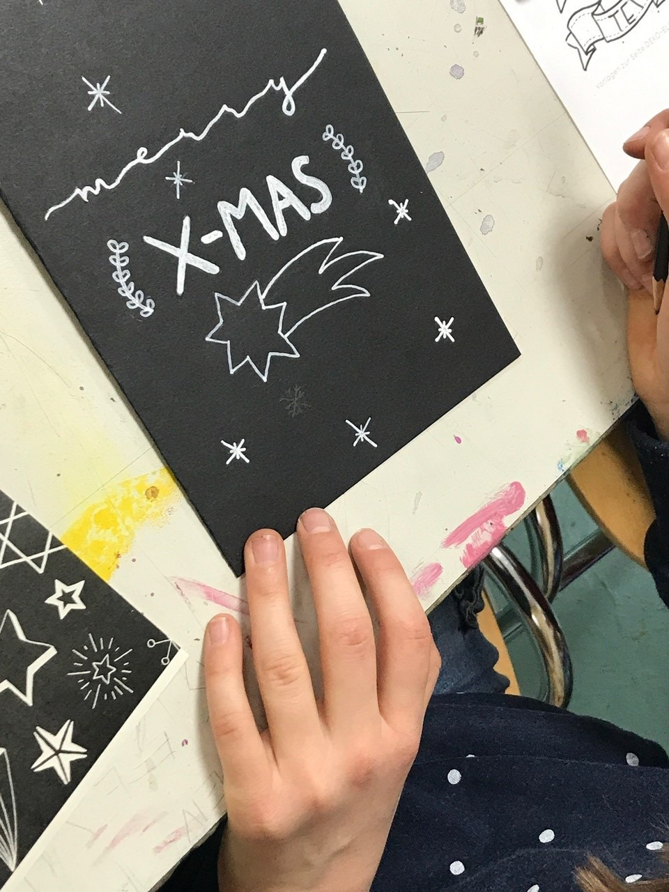 Ein schwarzes Blatt auf dem in silbernen Buchstaben Merry X-Mas steht.
