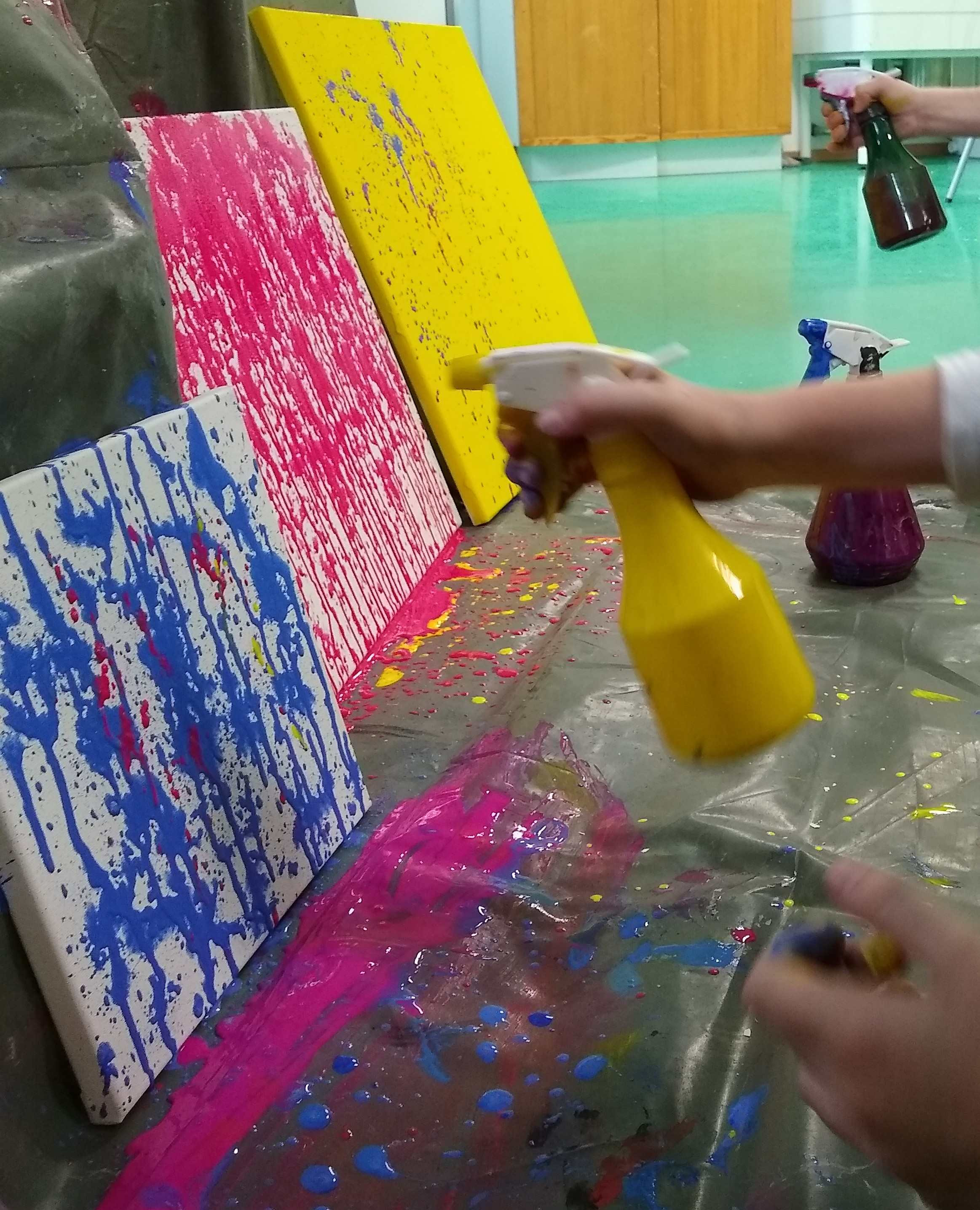 Mit Sprühflaschen wird Farbe auf eine Leinwand gespritzt.