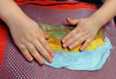 Zwei Kinderhände, die auf nasser flach ausgebreiteter Wolle in bunten Farben reiben