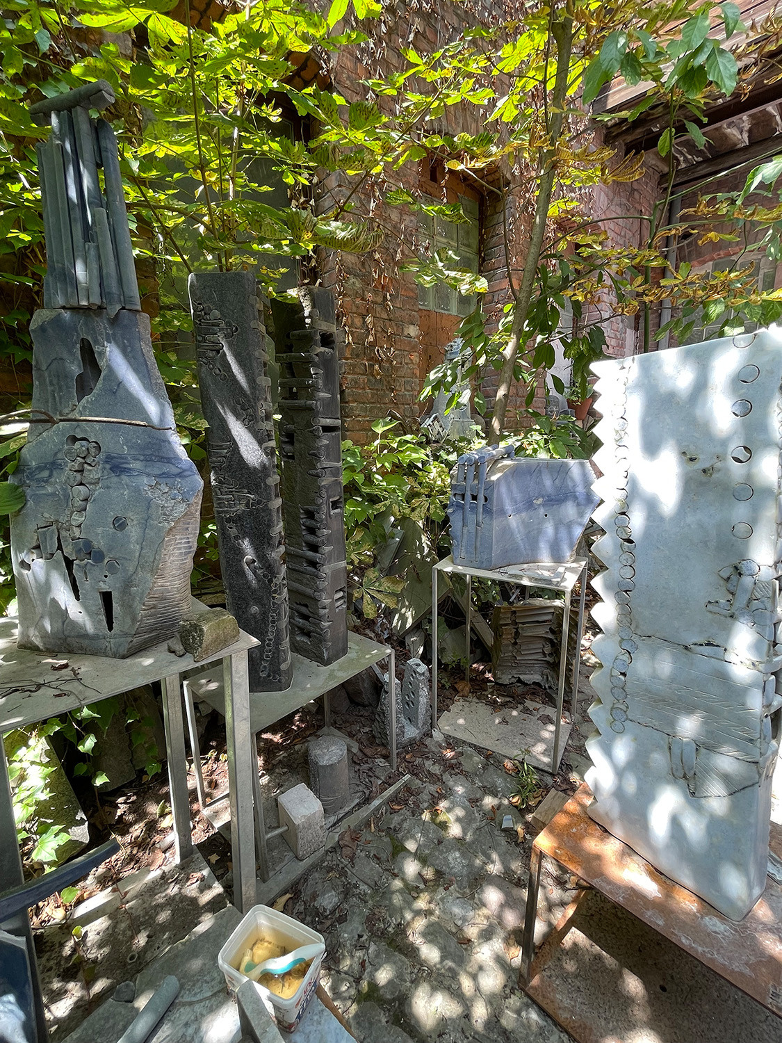Skulpturen aus Stein stehen in einem Hinterhof auf Holzregalen und Arbeitstischen