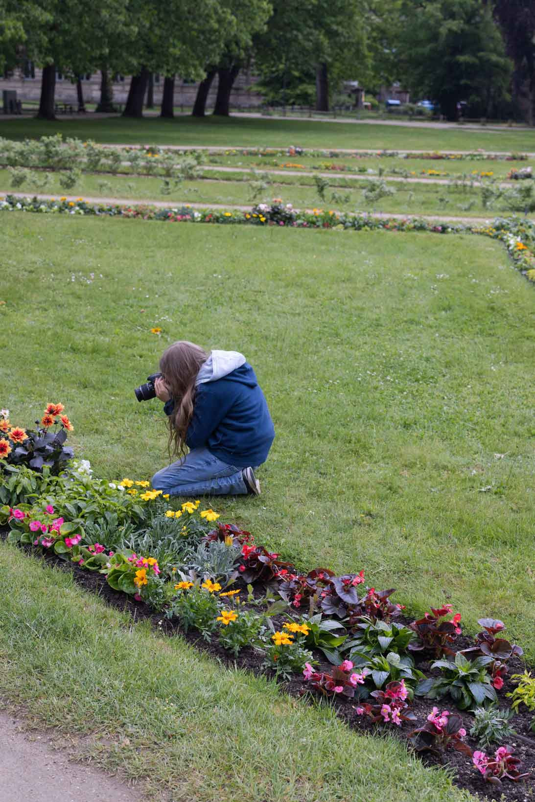 Ein Mädchen sitzt auf der Wiese und fotografiert Blumen.