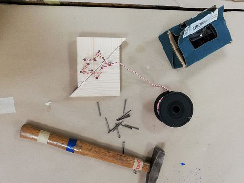 Vogelperspektive auf Werktisch mit Hammer, Nägel, 2dreieckigen Holzstücken die mit einer genagelten Sternform verbunden sind