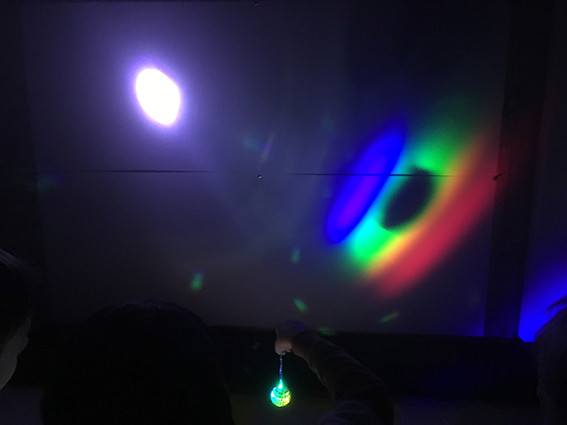 kreisrundes Lichtfarbspektrum im dunklen Raum, durch einen kleinen diamantgeschliffenen Glaskörper an die Wand gestrahlt