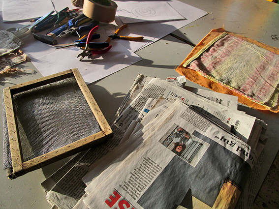Arbeitsplatz mit Materialien wie altes Zeitungspapier, Sieb, Zange, Stifte, Klebeband und mehr