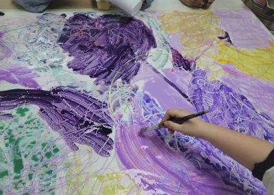 Mit einem Pinsel mal ein Kind großflächig lila farbene Felder auf ein Blatt Papier